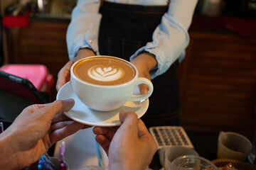 Fototapeta na wymiar two Hand put a Latte arts coffe hot coffee on wooden table.barista love art concept.