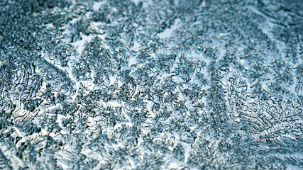 A pattern of ice crystals close-up on a window glass. Blue winter background or wallpaper. Frozen water. Backdrop for Christmas or New Year. Weather forecast: frost, cold snap. Strong macro