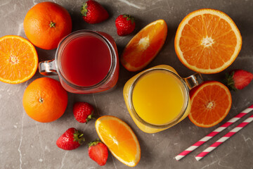 Glass jars with strawberry and orange juices on gray background