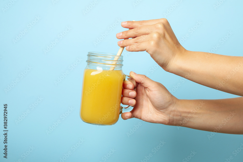 Wall mural Female hands hold banana juice on blue background