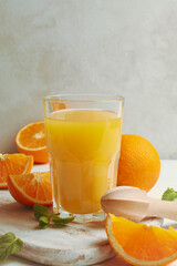 Board with glass of orange juice, oranges and juicer on wooden background