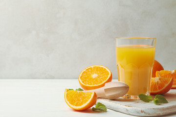 Board with glass of orange juice, oranges and juicer on wooden background