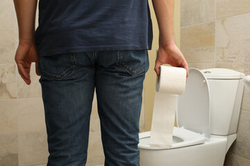A man stands near the toilet and holds toilet paper