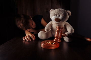 Divorce and separation concept. Wooden gavel, rings and sorrowful little boy with teddy bear.