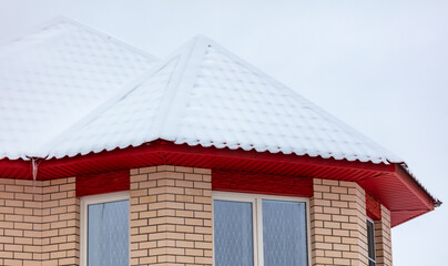 White snow lies on the red roof of the house.