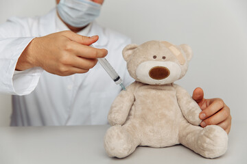 Male pediatrician makes an injection for sick teddy bear. Child healtcare and treatment concept.
