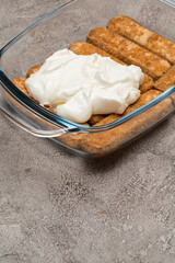 tiramisu dessert cooking - Traditional Italian Savoiardi ladyfingers Biscuits and cream in glass baking dish on concrete background