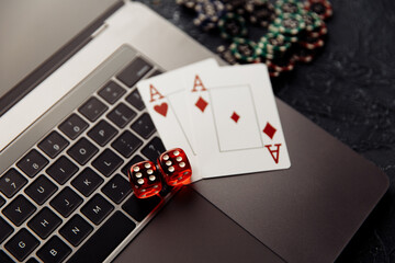 Chips, red dices and playing cards with aces for poker online or casino gambling on laptop keyboard top view. Online casino concept.