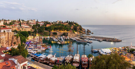 Fototapeta premium Panorama of the old city in Antalya, the old port in the harbor are yachts and ships, evening illumination of the city