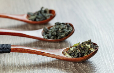 green tea leaves in a spoons on wooden background