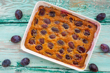 Homemade pie with plums on a wooden background.