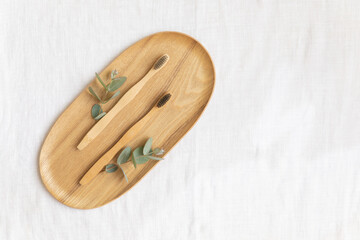 Bambool toothbrush and leaves of eucalyptus on a wooden plate.