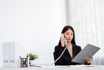 Asian businesswoman talking on the phone and working with a cheerful and happy smile while working at the office