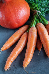 Carrots with fresh leaves and a pumpkin on dark background