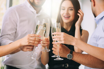 Young people clinking glasses of tasty champagne at party in office