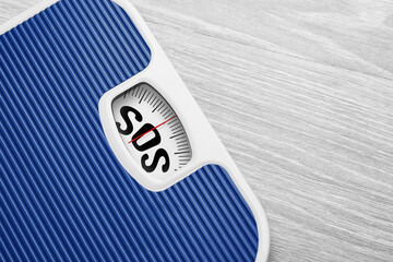 Scales with text SOS on wooden background, closeup. Weight loss concept