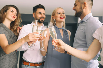 Young people clinking glasses of tasty champagne at party in office