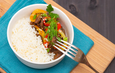 Roast beef with sweet pepper and white rice. White plate, garlic in the background, dark background.