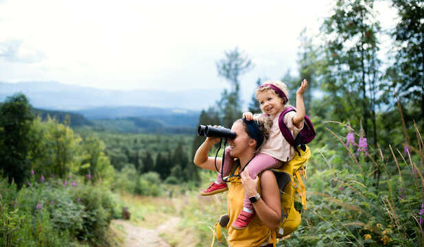 Mother with small toddler daughter hiking outdoors in summer nature, using binoculars.