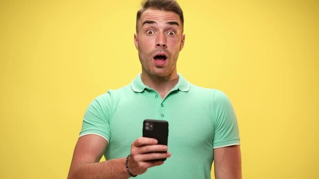 casual guy texting on his phone then being shocked of what he sees, slapping his face, puffing cheeks on yellow background