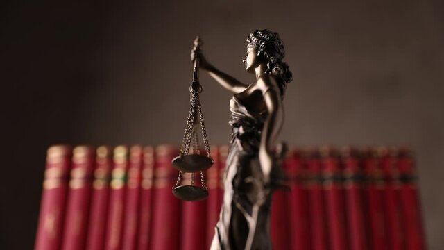 international bronze symbol of law represented by blindfolded goddess holding a balance signifying two broad sources of law, spinning slowly in front of red books on brown back