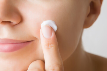 Young woman finger applying white moisturizing cream on cheek. Care about clean and soft face skin....