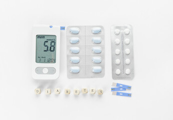 Glucometer with pills, strips and word DIABETES on white background