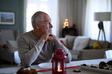 Lonely senior man sitting at the table indoors at Christmas, solitude concept.