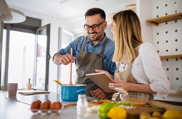 Happy young couple enjoys and having fun preparing healthy meal together at home kitchen.