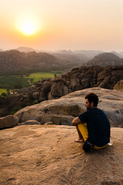 Seated adventurer staring at sundown in Monkey Temple surrounded by rice fields in Hampi. Travel, adventure, landscape, India, Karnataka.