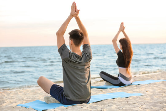 Sporty young couple practicing yoga on sea beach