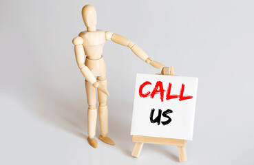 Wooden man shows with a hand to white easel with text CALL US on white background