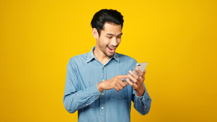 Asian man holding mobile phone and surprising while standing isolated on yellow background, People on smartphone, technology lifestyle