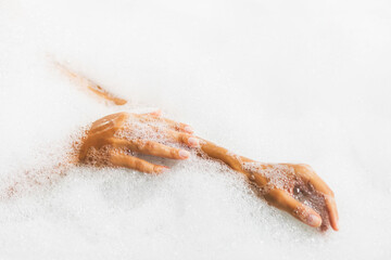 Woman hands in bath full of foam bubbles close-up. Spa beauty treatment.