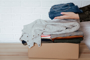Woman folding and packing clothes into cardboard donation box. Concept of volunteering work,...