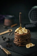A stack of fresh vegan chocolate waffles with banana slices on top. 