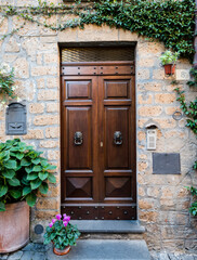 Old wooden door to the entrance of multi-storey building decorated with plants and flowers on sandstone wall in Orvieto, Umbria, Italy