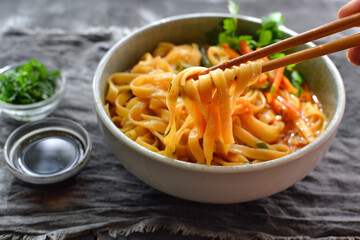 Noodles soup with carrots and parsley. Close up. Gray linen napkin. Wooden and concrete dark background. Egg noodles and Chinese sticks.