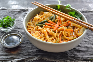 Noodles soup with carrots and parsley. Close up. Gray linen napkin. Wooden and concrete dark background. Egg noodles and Chinese sticks.