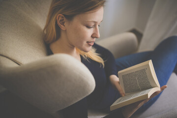 Cute young woman reading a book in a designer chair - color toned image, shallow DOF