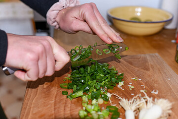 Chopping and preparing spring onion bunch with a sharp knife on a cutting board as an ingredient for a meal in the kitchen