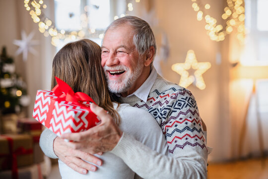 Young woman giving present to happy grandfather indoors at home at Christmas.