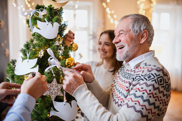 Multi-generation family indoors at home at Christmas, decorating tree.