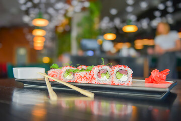 Salmon and caviar sushi rolls served on a traditional plate on a wooden table in a restaurant.