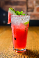 Watermelon smoothie garnished with watermelon slices and mint leaves served in a glass on rustic wooden table.