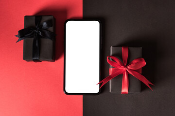 Black Friday sale shopping concept, Top view of gift box wrapped in black paper and black bow ribbon and modern mobile smartphone, studio shot on red and dark background