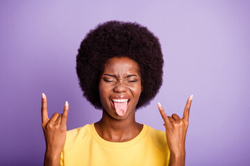 Portrait of crazy dark skin girl make horned symbol show tongue wear yellow sweater isolated over purple color background