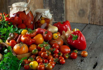 Tomatoes, peppers, onions on the table. Preservation of the autumn harvest of vegetables. Glass jar with pickled tomatoes. Wooden background. Vegetable food. Still life. Copy space.