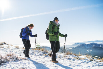 Senior couple with nordic walking poles hiking in snow-covered winter nature.