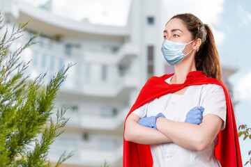 A young female doctor wearing a surgical mask and rubber gloves poses with her arms crossed and a...